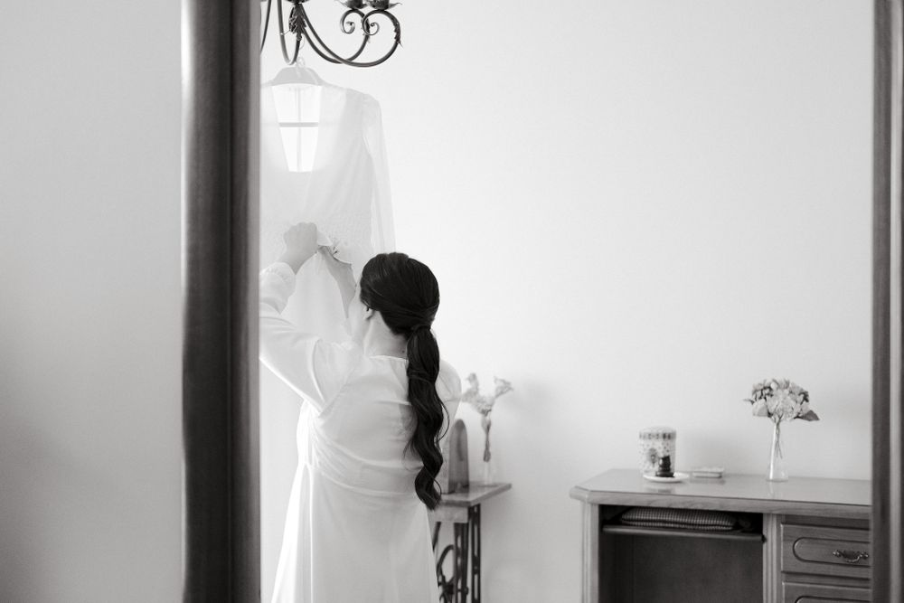 Silhouette of bride in white dress standing by window in black and white.