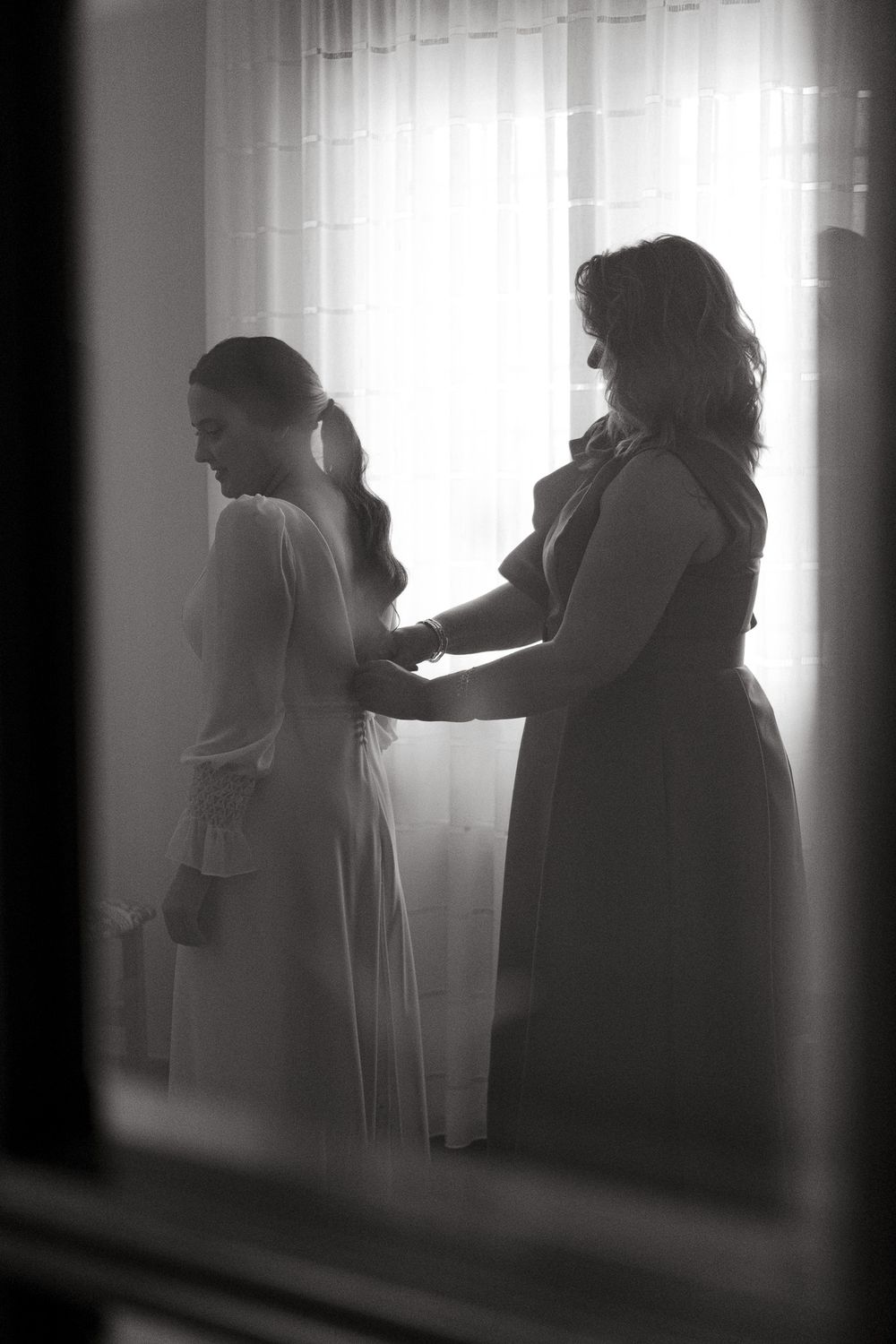 Black and white image of wedding dress preparations through doorway.