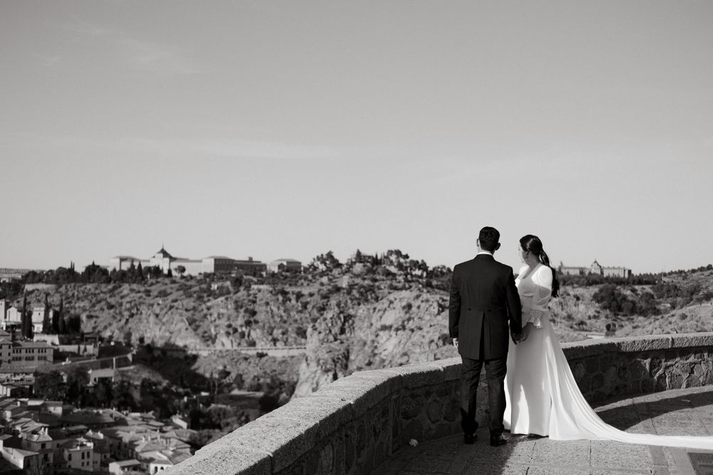 Wedding couple stands overlooking an ancient city landscape from a scenic stone viewpoint.