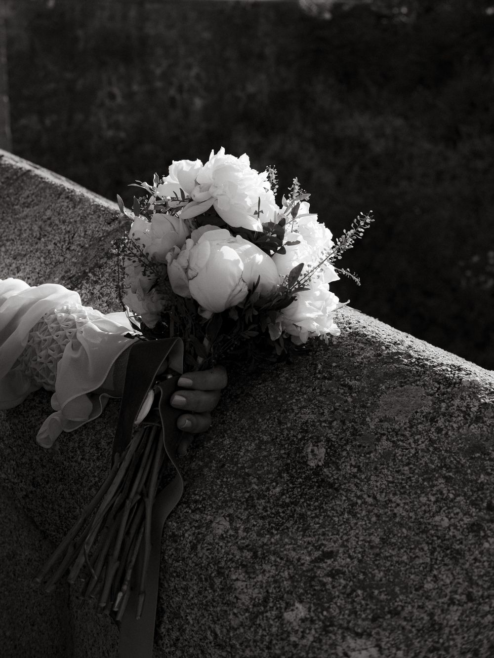 Elegant white peony bridal bouquet resting on stone ledge in black and white.
