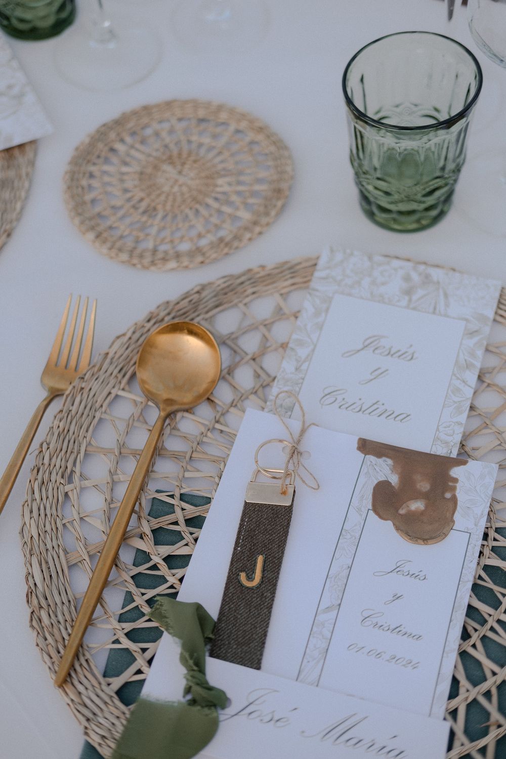 Elegant wedding place setting with gold cutlery, green glassware and detailed menu card.