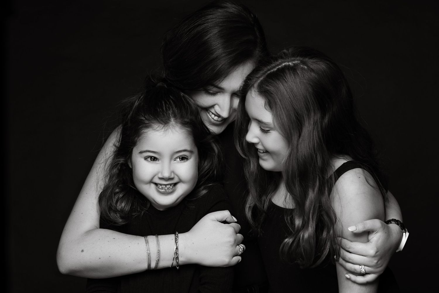Three people sharing a joyful embrace while wearing black in dramatic black and white portrait photography.