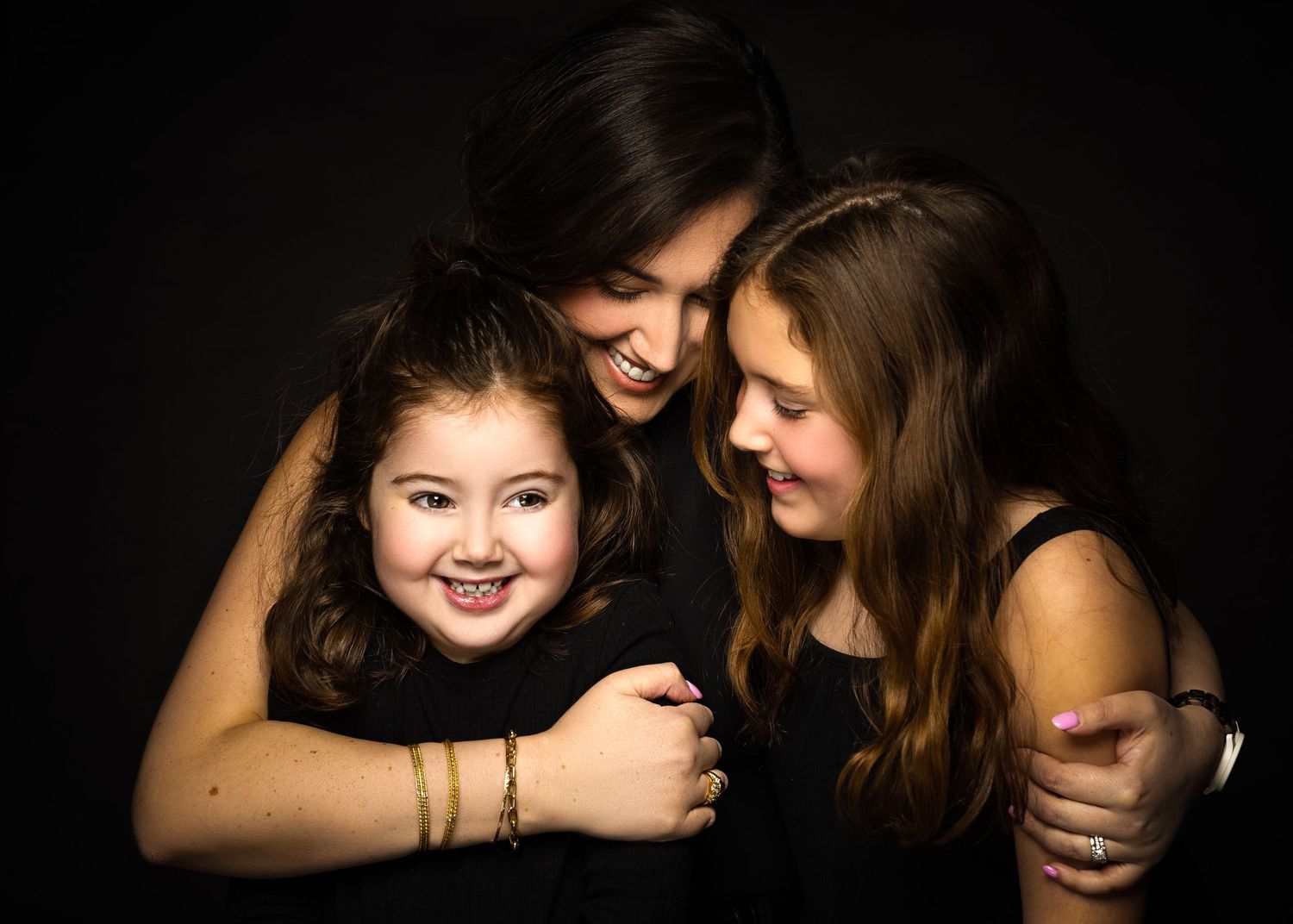 Three people sharing an intimate moment of joy and laughter against a dark background in a studio portrait.