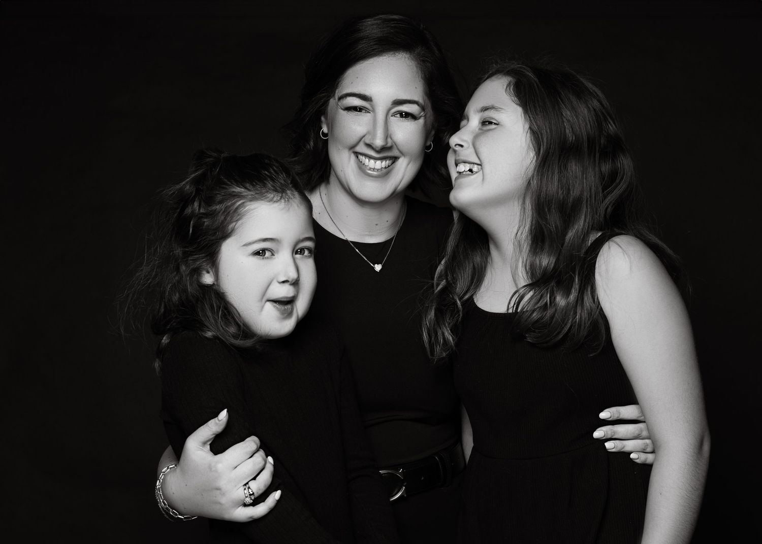 A black and white portrait of three people sharing a joyful moment together, all wearing black clothing.