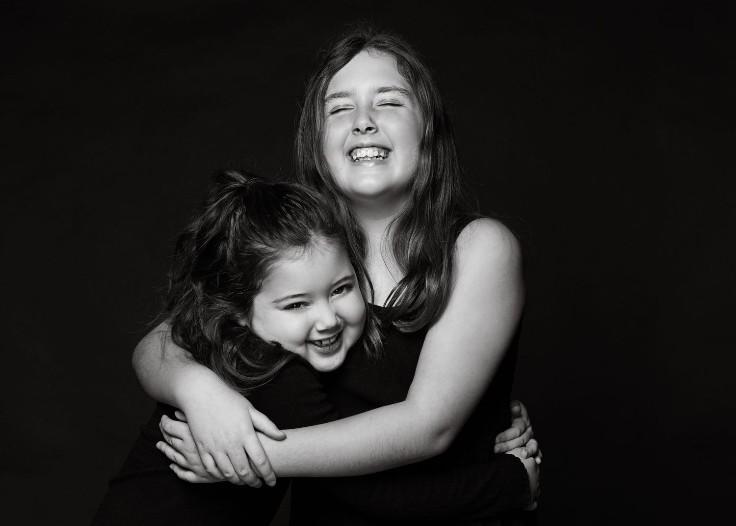 Black and white portrait of two people sharing a joyful embrace against a dark background.