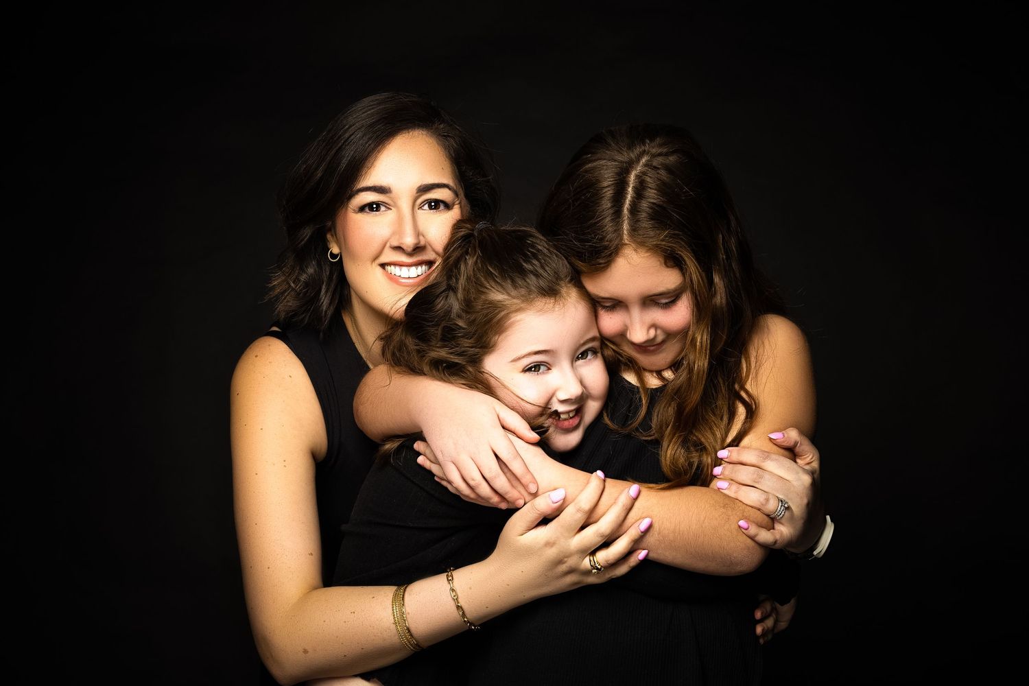 Three people in black outfits share laughter and hugs during intimate portrait session.