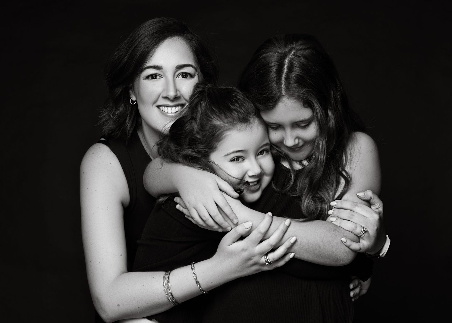 Black and white portrait of three people embracing and laughing together in a joyful moment.