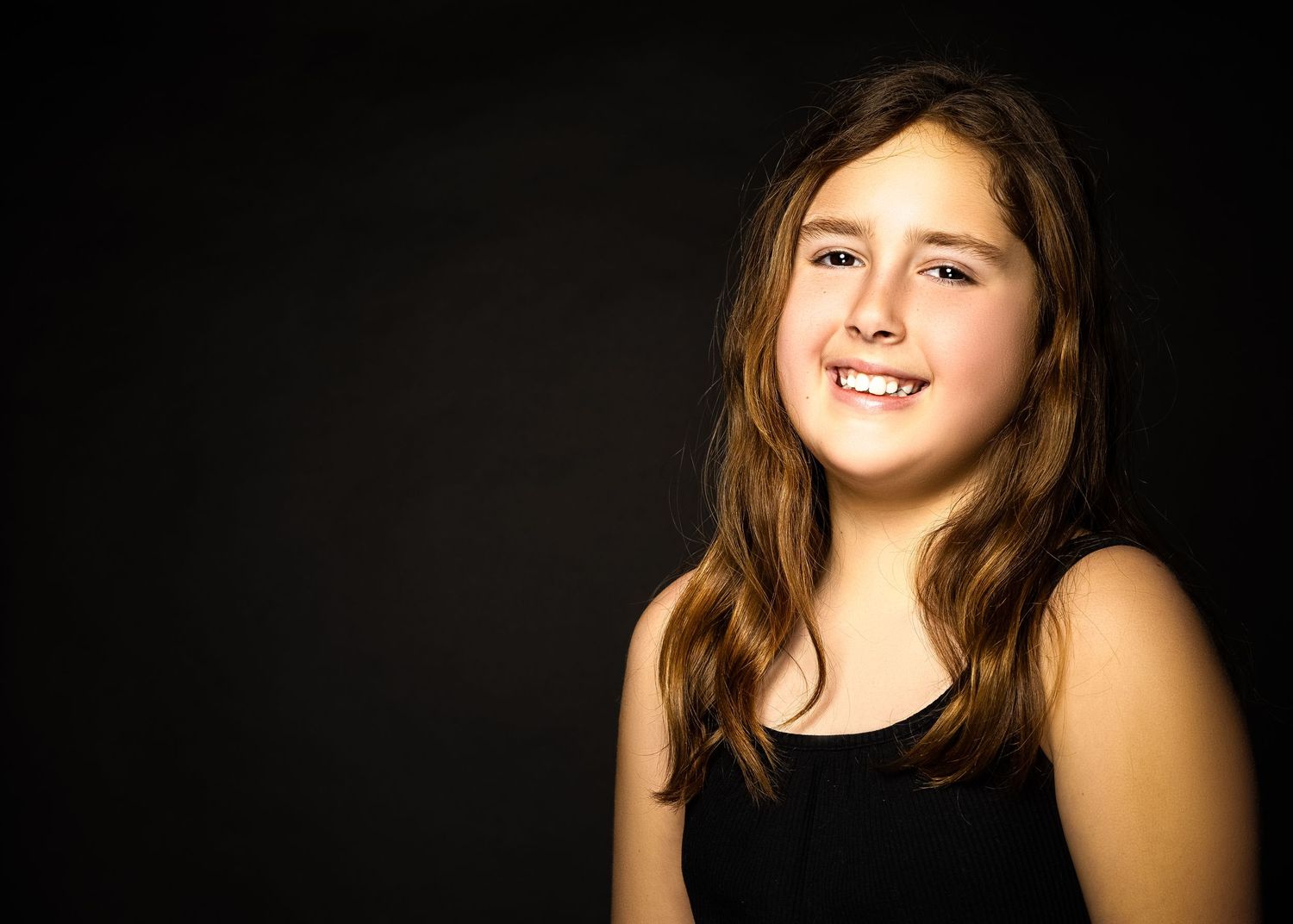 Portrait of person in black tank top smiling warmly against dark background.