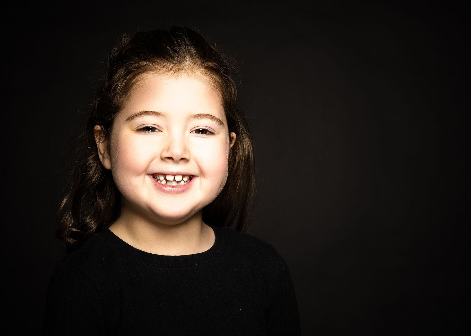 Close-up studio portrait showing a cheerful expression against a dark background.