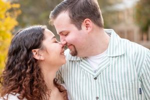 A tender moment between a couple in white and striped clothing against autumn foliage.