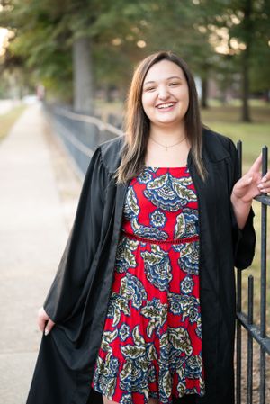 Cheerful portrait in a black cardigan and red patterned dress standing by a metal fence.
