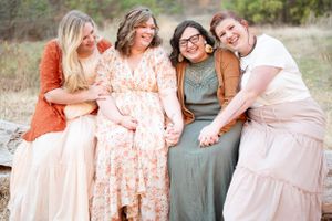 Four friends sitting together outdoors in coordinated pastel and neutral-toned dresses.