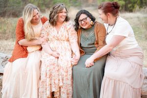Group of friends sitting together outdoors wearing coordinated earth-toned dresses.
