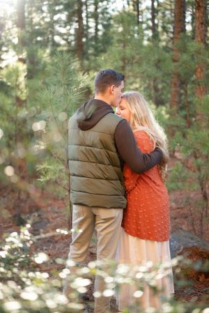 A couple embracing in a pine forest wearing casual fall clothing.