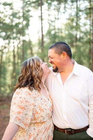 A joyful couple sharing a laugh together in a sunlit forest setting.