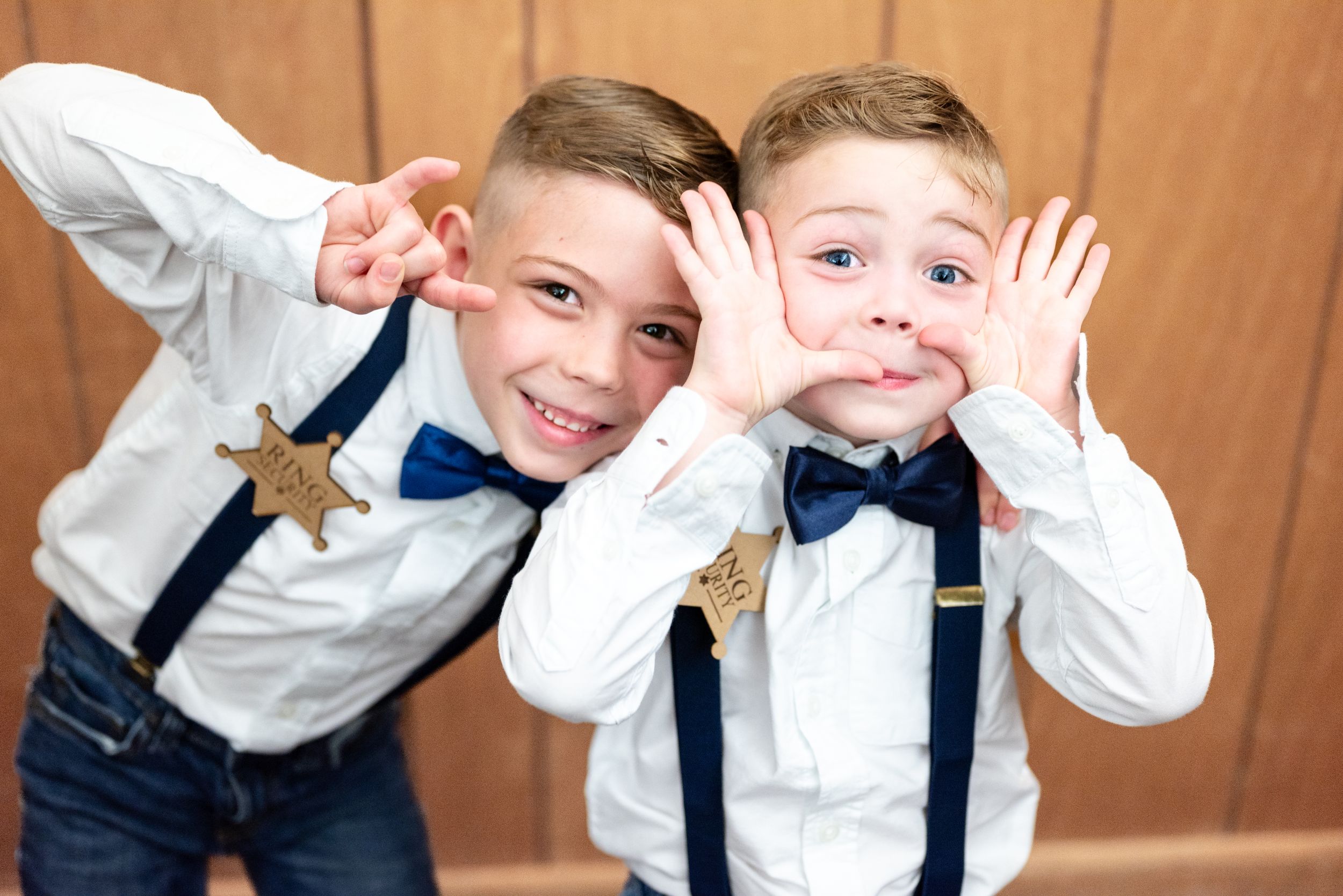Two young ring bearers in matching outfits making playful faces at camera.