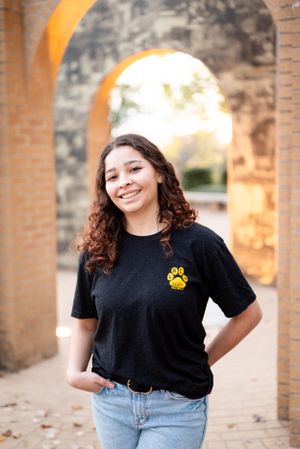 Portrait of someone in casual attire smiling near brick archways in warm sunlight.