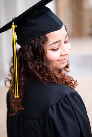 Graduate wearing black cap and gown with gold tassel poses with curly hair and warm smile.