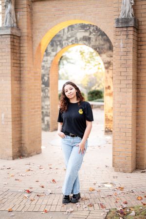 Portrait through brick archway with autumn foliage wearing casual black t-shirt and jeans.