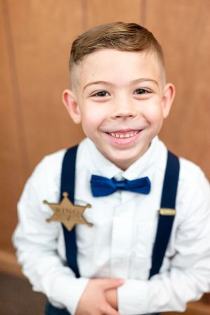 Young ring bearer in crisp white shirt, navy bow tie and suspenders with sheriff badge.