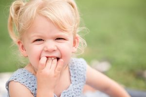 A joyful moment captured outdoors as light falls on a blue dress and green background.