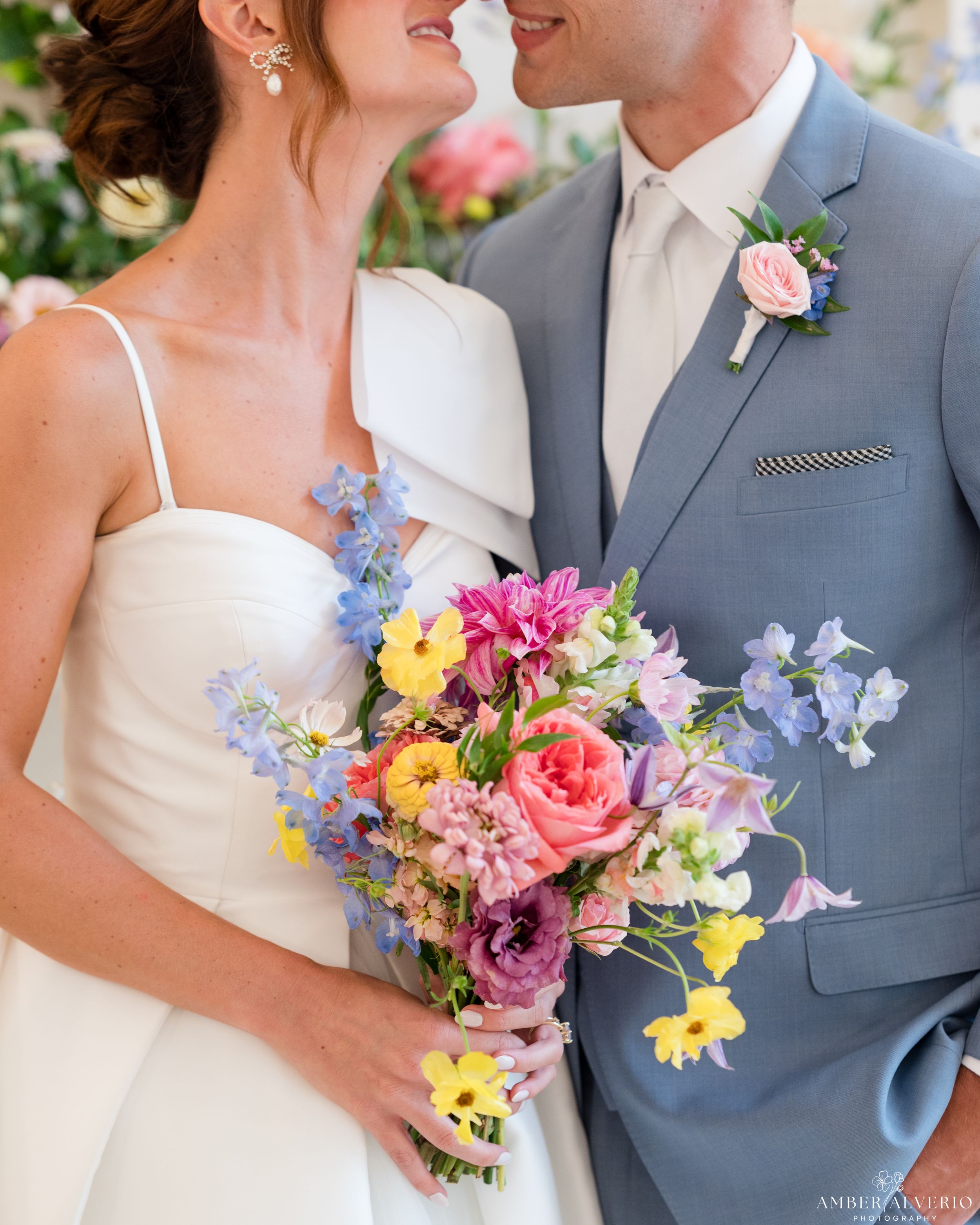 Colorful spring wedding bouquet with pink roses and blue delphinium against formal attire.