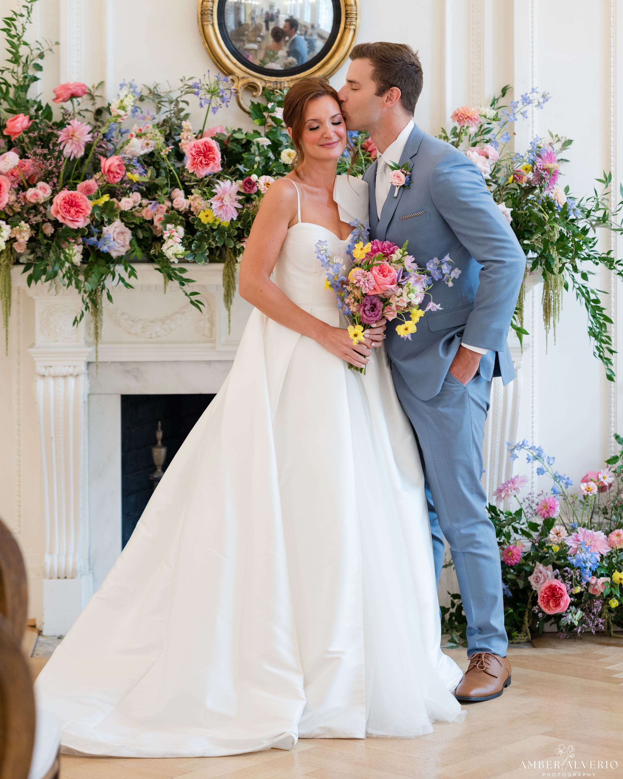 Elegant wedding ceremony setup with floral arch and couple in front of white fireplace.