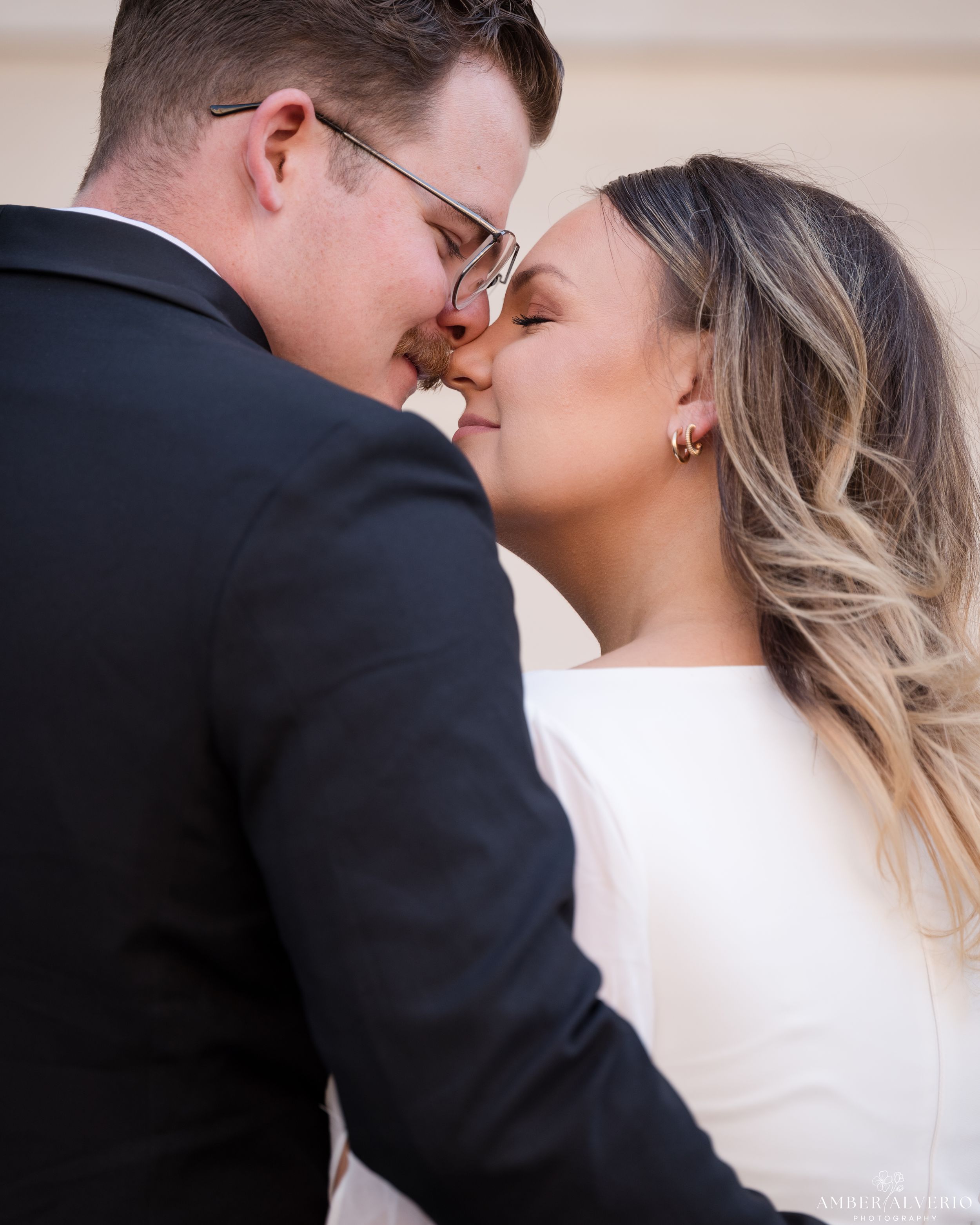 A romantic portrait of a newlywed couple sharing an intimate kiss at a wedding, bride in white and groom in black suit.