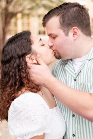 A romantic kiss shared between a couple in casual attire against a blurred background.