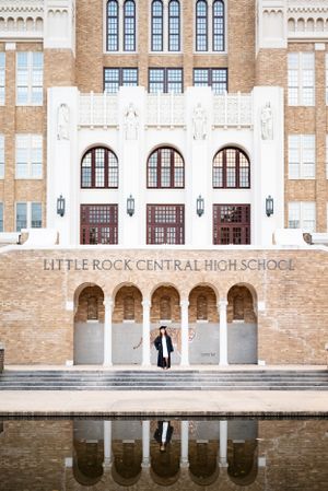 Little Rock Central High School's historic facade with graduate posing on front steps by reflection pool.