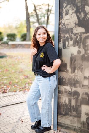 Casual portrait against historic photo wall wearing black t-shirt with logo and light jeans.