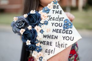 Graduation cap decorated with blue roses and inspirational teaching quote.