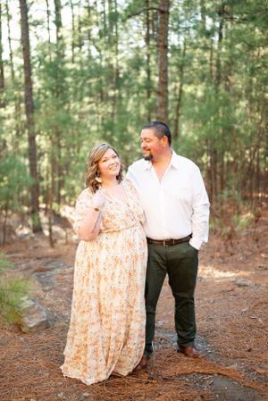 A couple in coordinated outfits sharing a tender moment on a pine needle-covered forest path.