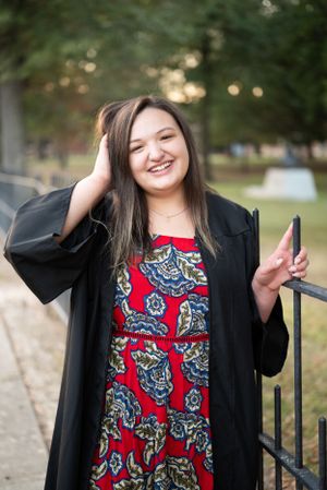 Casual portrait in a black cardigan and patterned red dress near an iron fence.