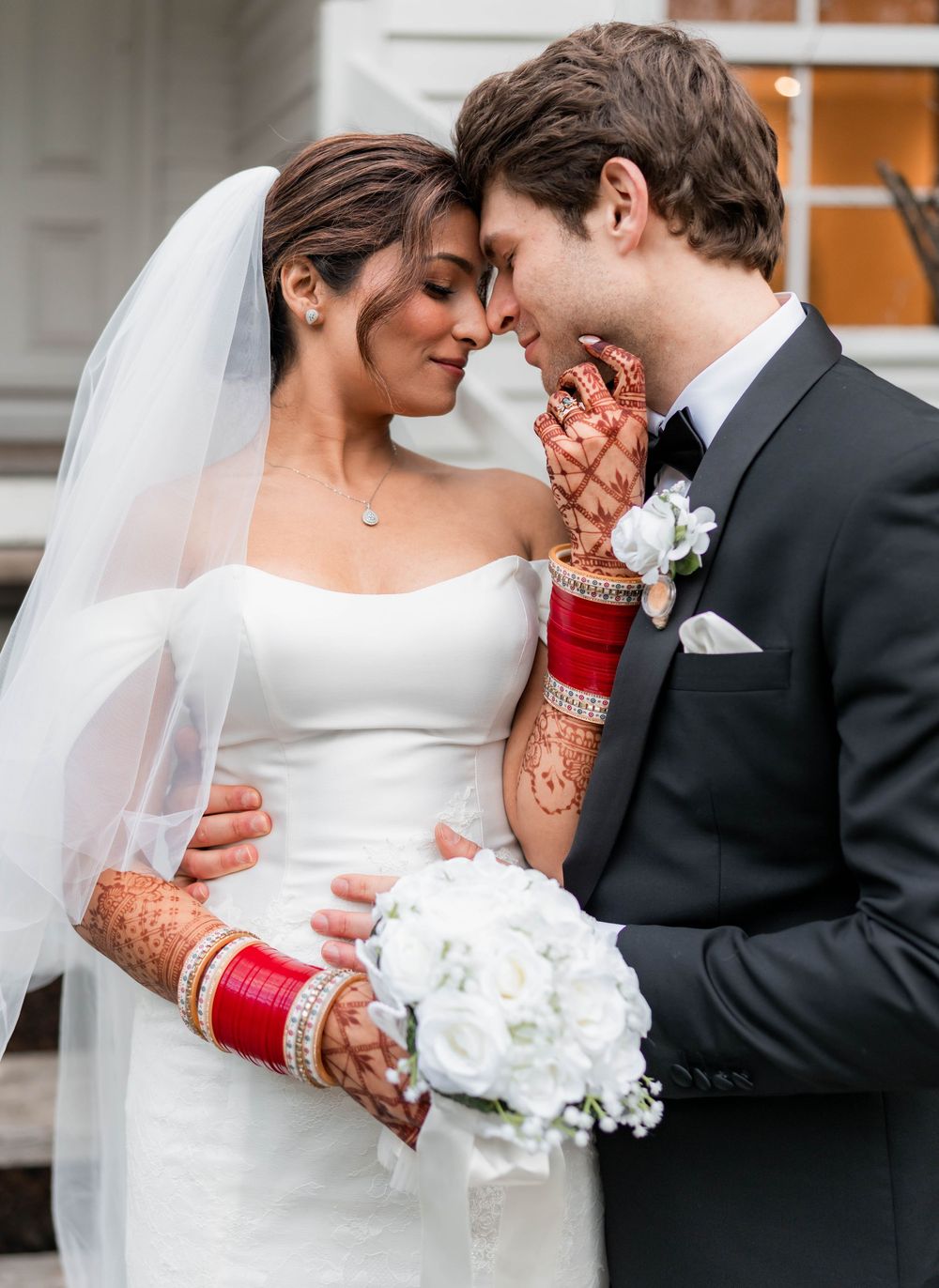 Romantic wedding couple in intimate embrace with bride wearing white dress and traditional red bridal bangles.