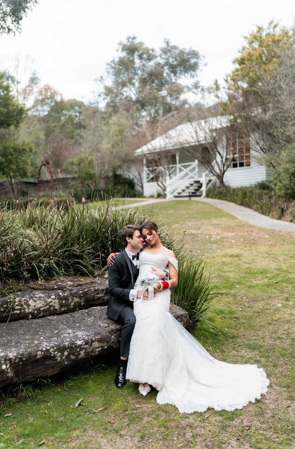 A romantic wedding couple shares intimate moments on grassy grounds near a white building.