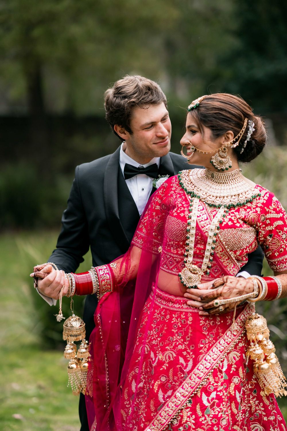 A couple in formal wedding attire, with the bride wearing a stunning red and gold traditional South Asian lehenga.