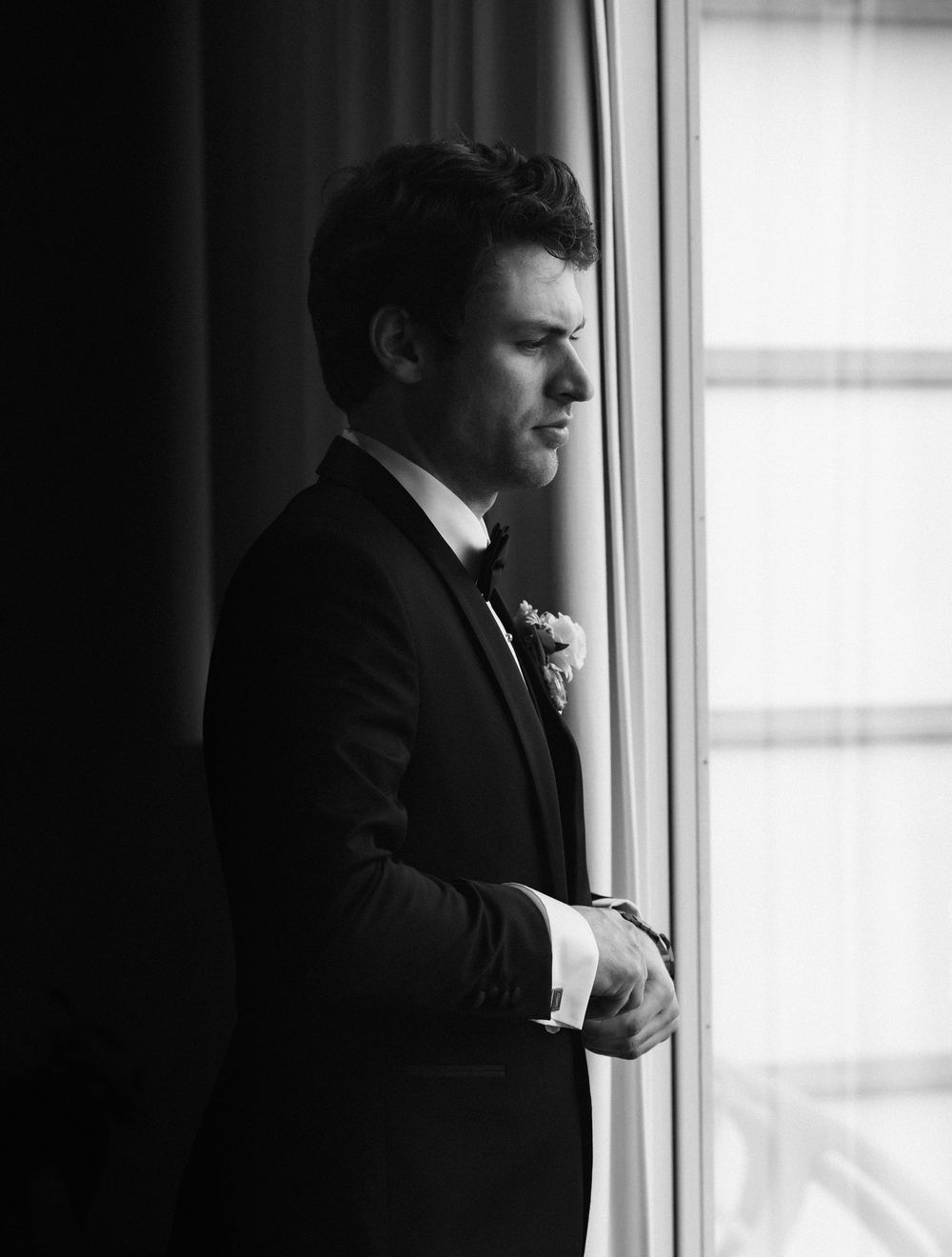 A silhouetted figure stands by a bright window in a black suit, creating a dramatic contrast in black and white photography.