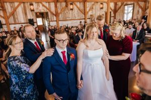 A joyful celebration during a rustic barn wedding ceremony with guests gathered around the couple in formal attire.
