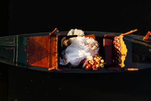 A romantic couple sits in a wooden gondola at night, adorned with flowers and soft lighting.