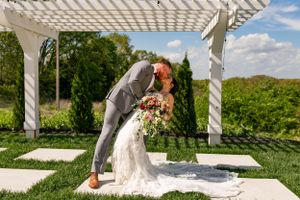A newlywed couple shares a tender moment under a white pergola in a lush garden setting on their wedding day.