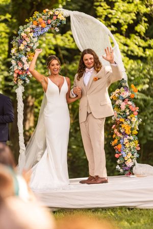 Newlyweds celebrate under a colorful floral arch during an outdoor wedding ceremony.