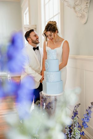 A couple sharing a joyful moment together while cutting their elegant light blue tiered wedding cake.