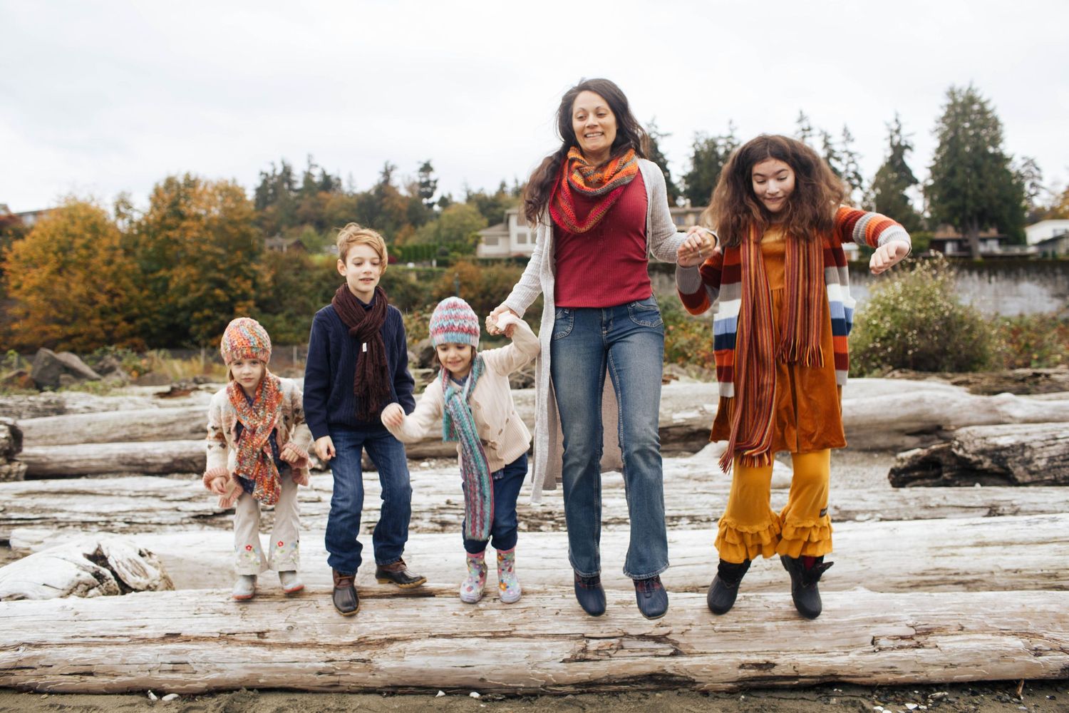 Everett family photographer: A mother with her kids jump off a piece of driftwood at Edgewater Beach Park in Mukilteo WA