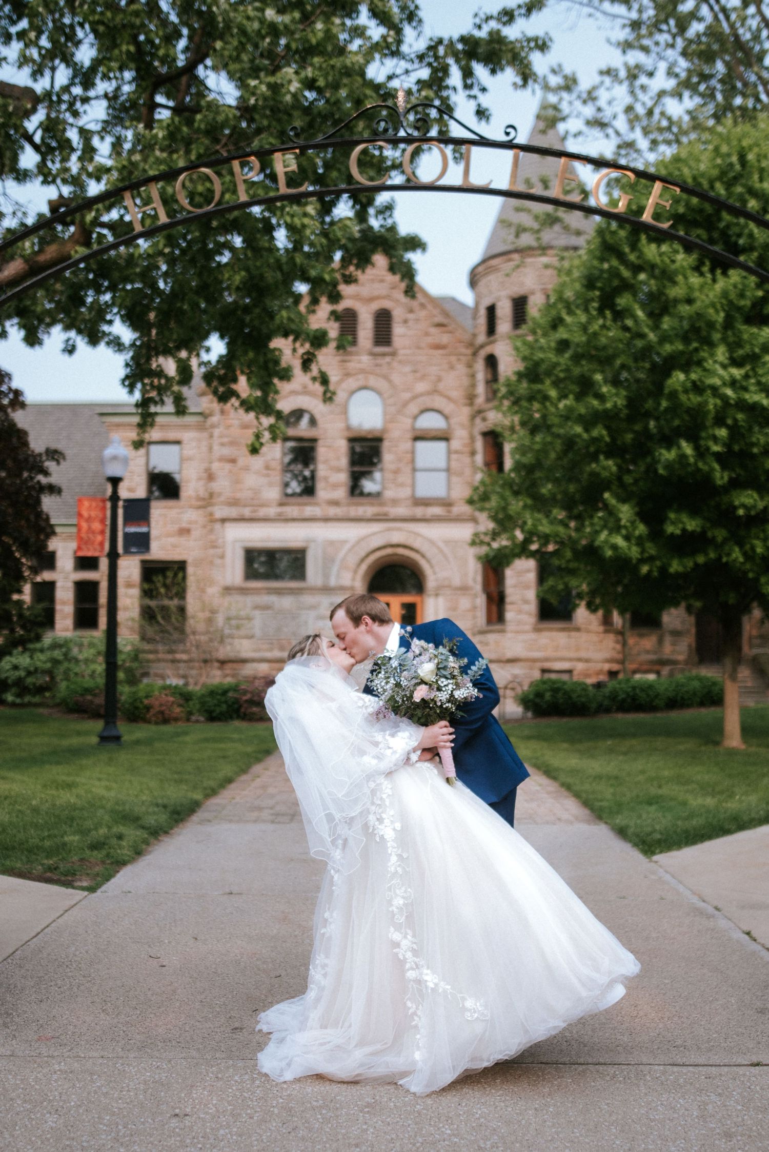 A romantic wedding couple embraces in front of historic Ashmore College building with stone architecture and arches.