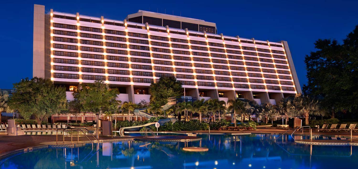 Modern resort hotel exterior at dusk with illuminated facade and swimming pool.