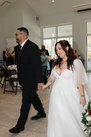 Bride in white gown and groom in black suit hold hands walking into wedding reception hall.