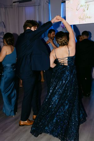 Couple dancing at a formal event, woman in navy sequin gown, man in dark suit, under blue ambient lighting.