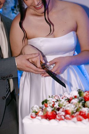 Bride and groom cutting a white wedding cake topped with fresh strawberries at their reception.