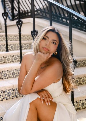 Young woman in white strapless dress sitting gracefully on ornate tiled steps with decorative iron railing.